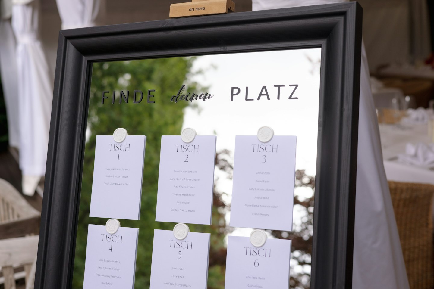 Plan stołów na lustrze z nazwiskami gości i pieczęciami lakowymi.
